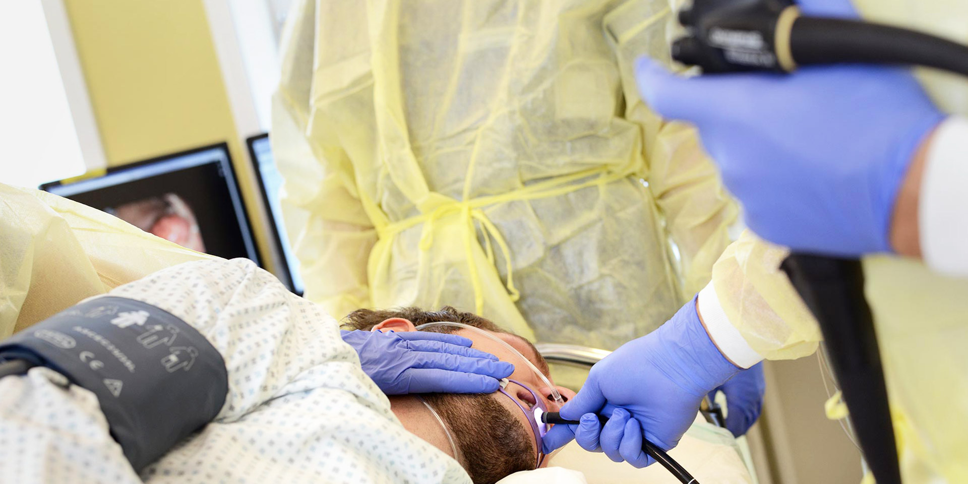 Patient liegt auf einer Behandlungsliege und Arzt führt ein Endoskop über den Mund des Patienten ein.