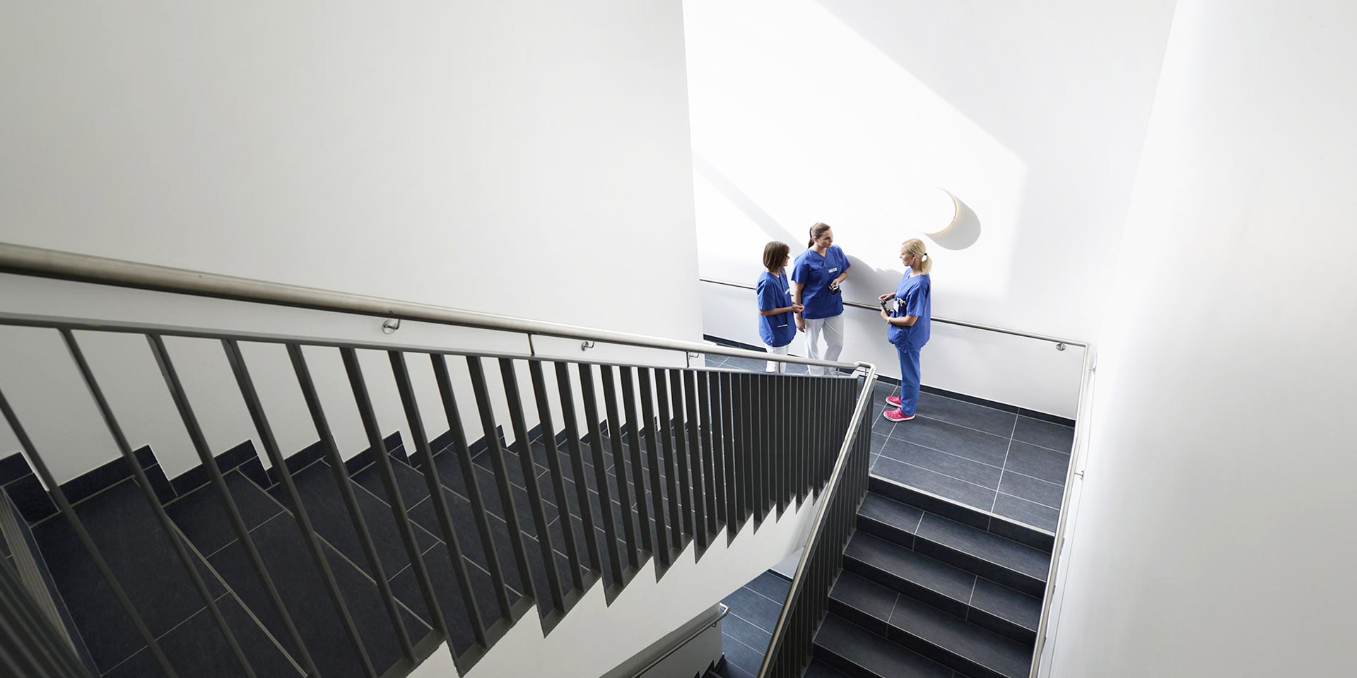 Drei Frauen in blauen Kasacks stehen im Treppenhaus des EVK Mettmann und unterhalten sich.