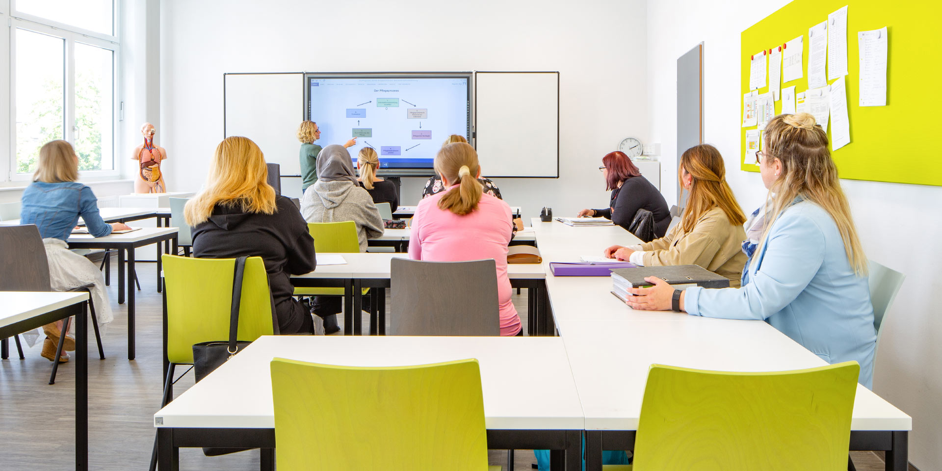 Lehrerin erklärt Auszubildenden etwas an einer digitalen Tafel im Klassenzimmer der Pflegeakademie.