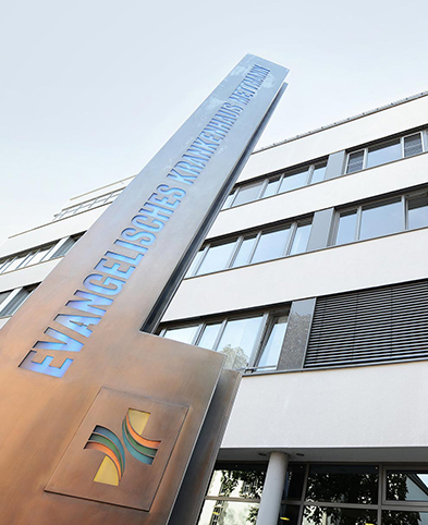 Außenansicht des Krankenhauses mit der Steele und dem Schriftzug Evangelisches Krankenhaus Mettmann – Blick Richtung Himmel.