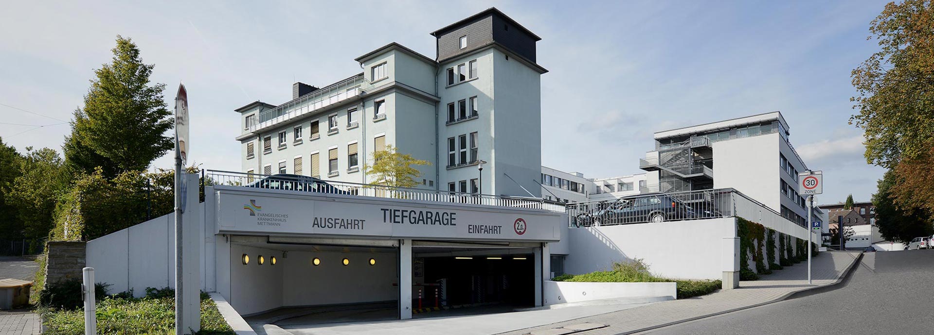 Blick zur Einfahrt der Tiefgarage des EVK Mettmann – im Hintergrund sieht man das Krankenhausgelände mit Neu- und Altbau.