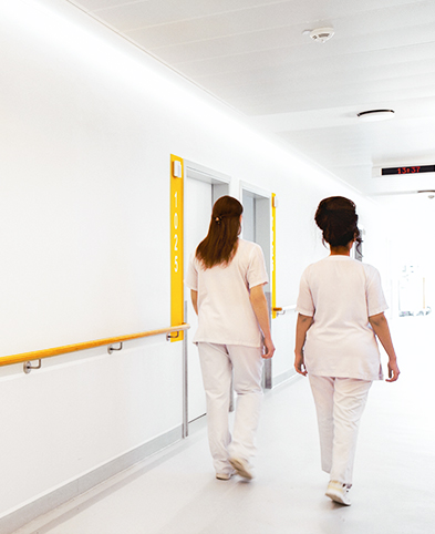 Zwei Pflegefachkräfte gehen entlang von Patientenzimmern auf der Station der Inneren Medizin.